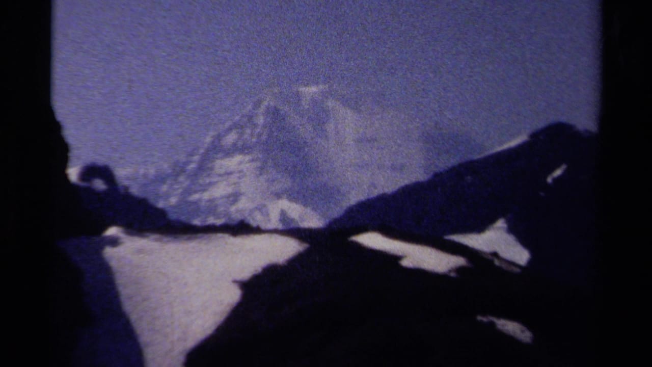 Mountain peak and snowfield framed by dark ridges and black film edge.
