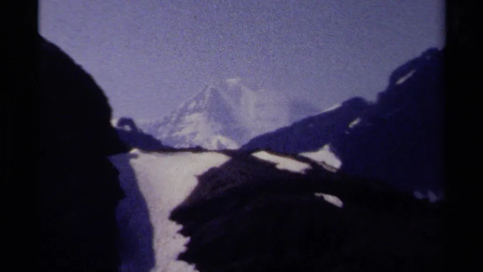 1979 home-movie frame with a distant snowy British Columbia peak partly blocked by dark alpine foreground shapes.
