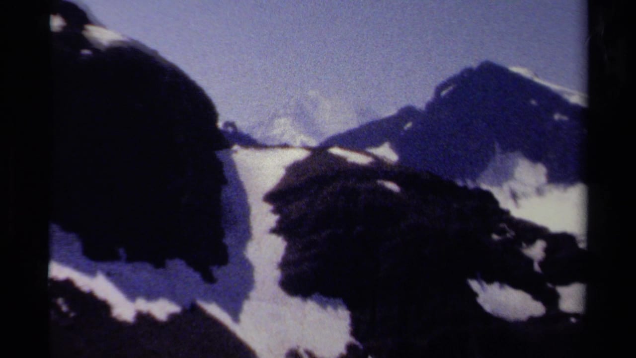 Snow-covered mountain ridges under a pale blue sky in a grainy 8mm frame.