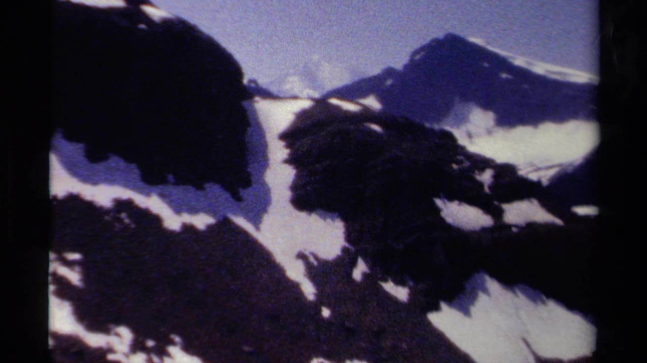 British Columbia alpine view on 8mm film, with shadowed rock faces, white snowfields, and distant mountain forms.