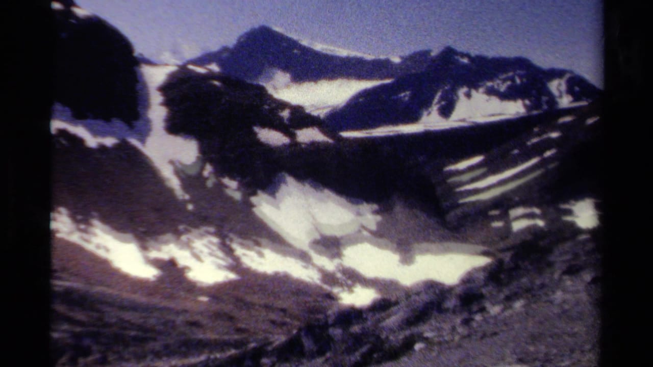 Snow-streaked mountain ridges under a blue sky, seen from a dark-edged 8mm frame.
