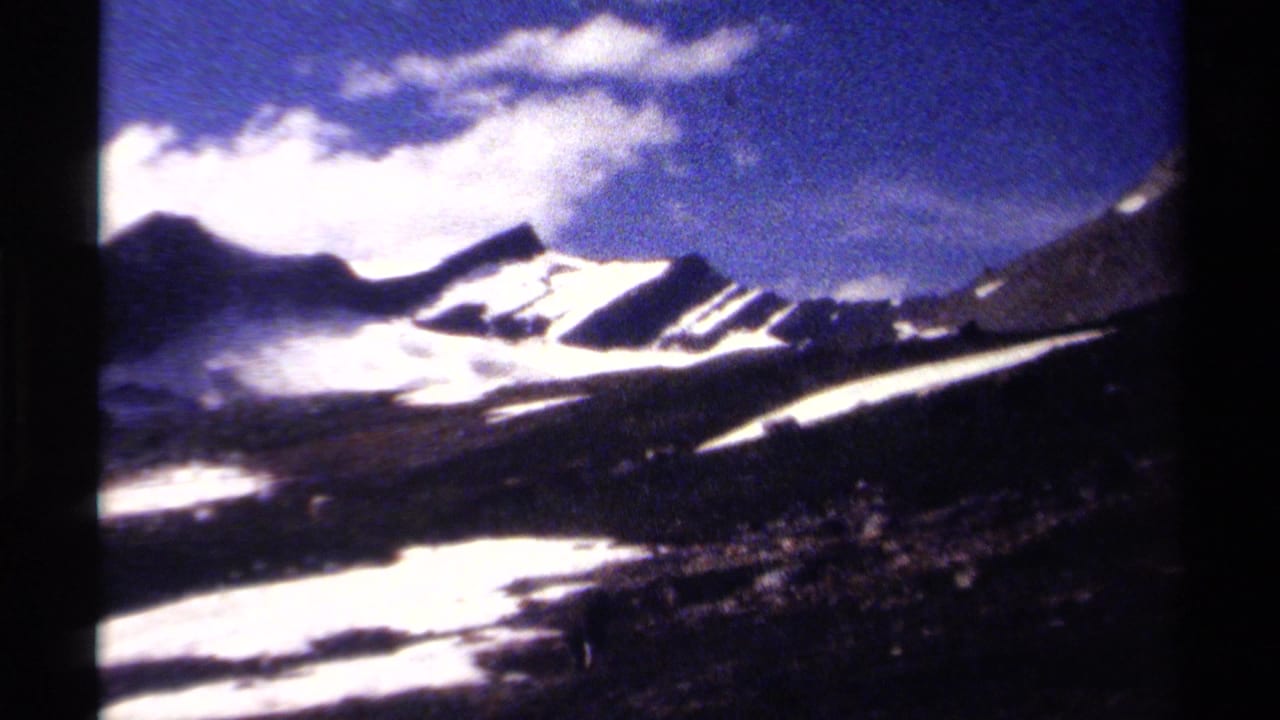 British Columbia mountain valley on 8mm film, showing bright snowfields, dark ridges, scattered clouds, and high-contrast alpine terrain.
