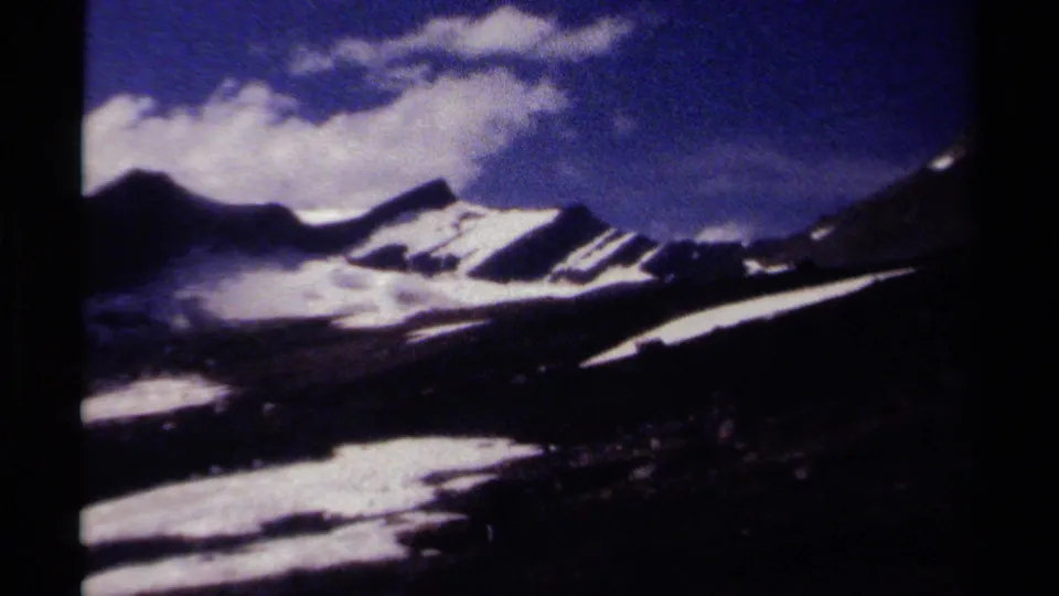 Handheld 1979 8mm alpine view in British Columbia, with snow patches across mountain slopes and a shadowed valley below.