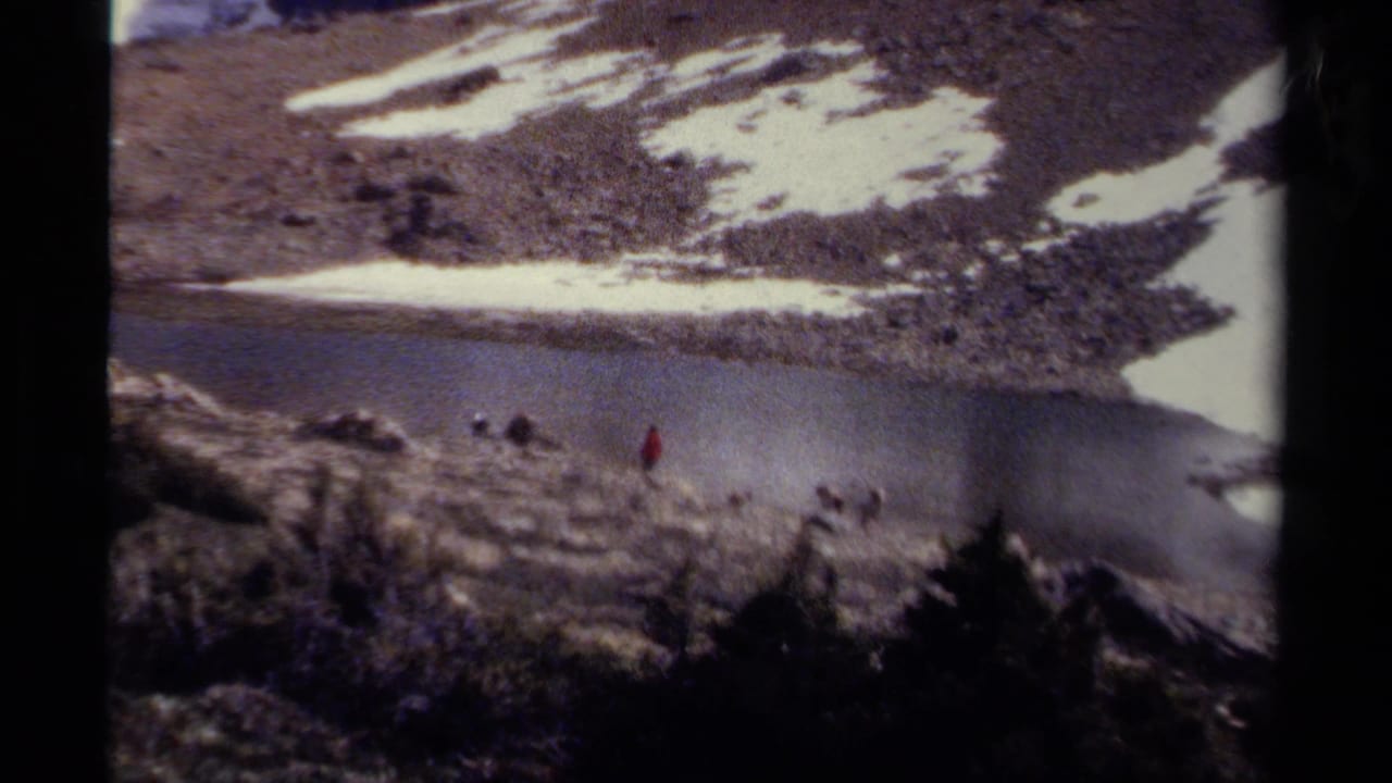 Small hiking group near a mountain lake with one figure in a red jacket.