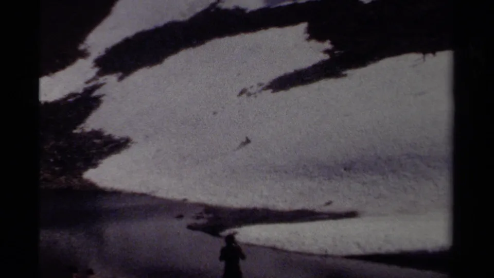 A silhouetted person stands near snow, rock, and meltwater in a British Columbia alpine landscape from 1979 8mm footage.