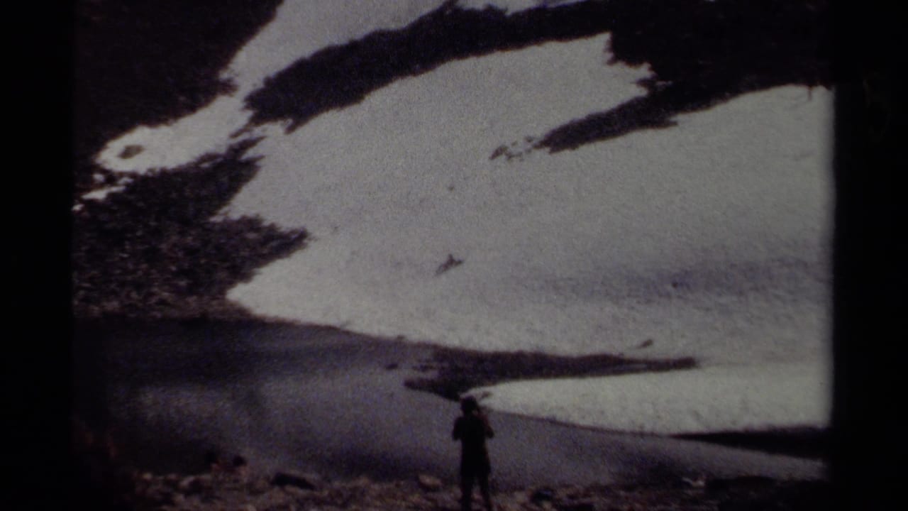 Person walking near a large snow patch and rocky mountain base.