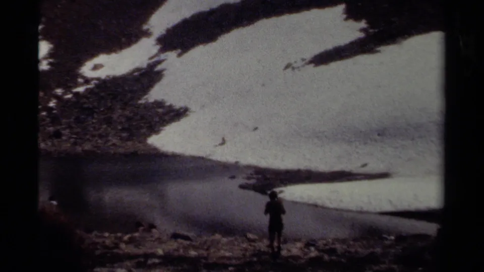 A lone person is seen near rocky ground, meltwater, and a broad snow patch in a 1979 British Columbia alpine scene.