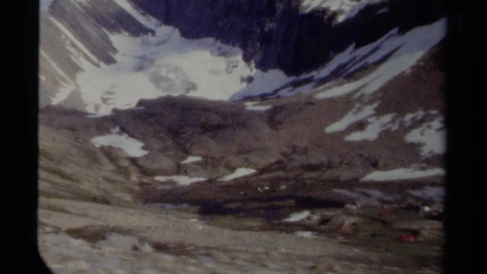 1979 British Columbia home-movie frame showing a rugged mountain basin with snow patches, rocky ground and a small lake or meltwater area near the base.