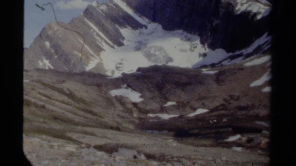 British Columbia mountain landscape on 1979 8mm film, showing ridged rock slopes, snowfields, glacier ice, sky, and visible scan marks.
