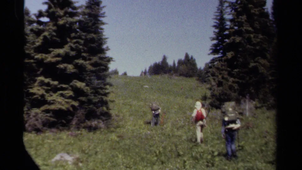 The hiking group continues uphill through the meadow, with backpacks visible and conifer trees framing the 1979 British Columbia scene.