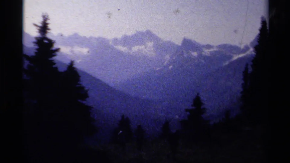 A hazy British Columbia mountain panorama shows layered ridgelines, evergreen silhouettes, and snow traces in handheld 8mm color.