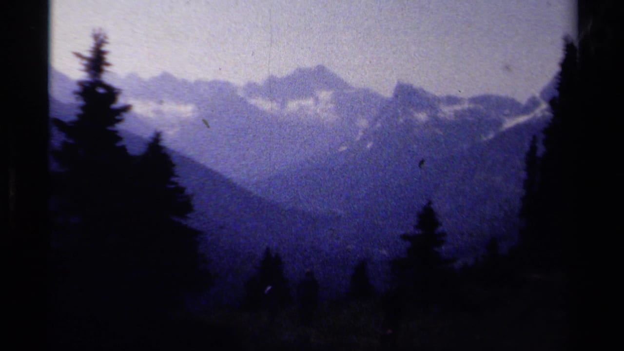 1979 8mm view in British Columbia showing evergreen silhouettes and distant mountain ridges under a cloudy sky.