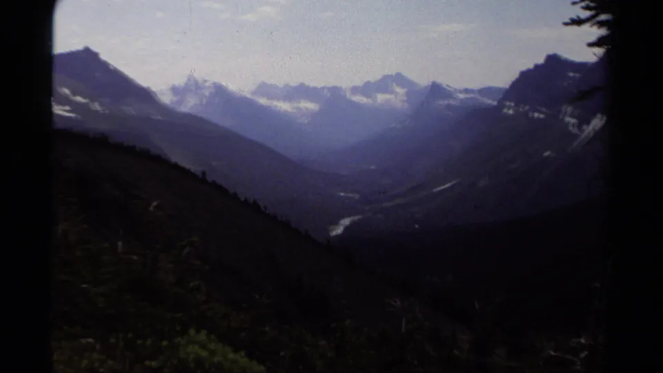 1979 8mm British Columbia mountain valley view with snow-streaked peaks, forested slopes, and a winding river far below.