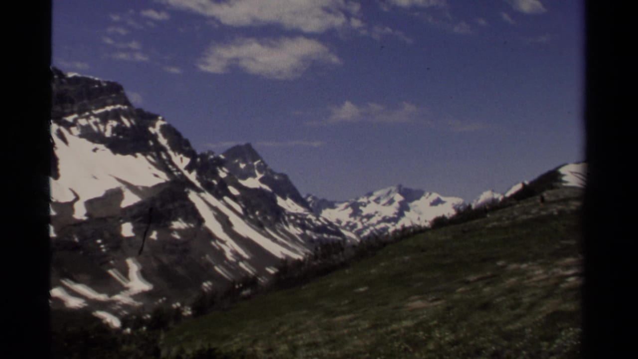 1979 8mm home-movie view of snow-streaked British Columbia peaks, grassy alpine terrain, and scattered clouds.