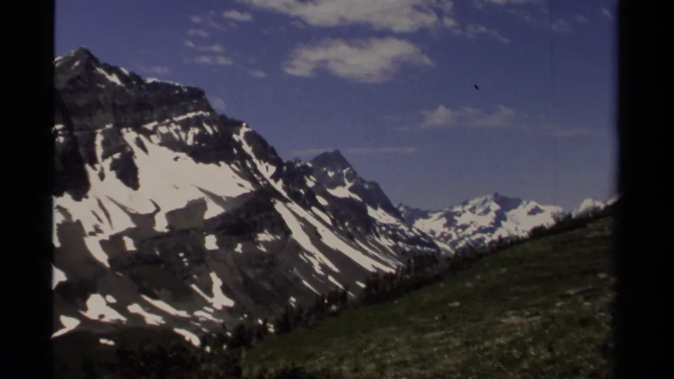British Columbia alpine landscape on 8mm film, with a snow-marked ridge, green hillside, and distant peaks.