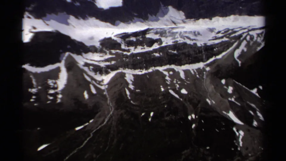 1979 British Columbia 8mm view of snow-streaked alpine ridges, dark rock faces, and a narrow drainage cutting through the slope.