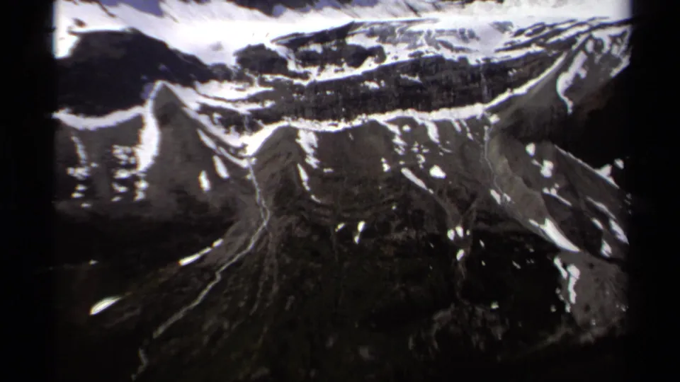 1979 British Columbia home-movie frame showing snow-streaked mountain slopes and rugged alpine terrain from an elevated viewpoint.