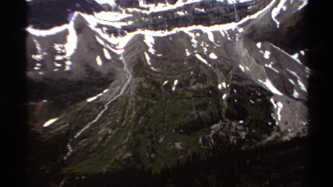 1979 British Columbia frame with steep mountain ridges, snow patches, and dark alpine terrain in soft 8mm color.