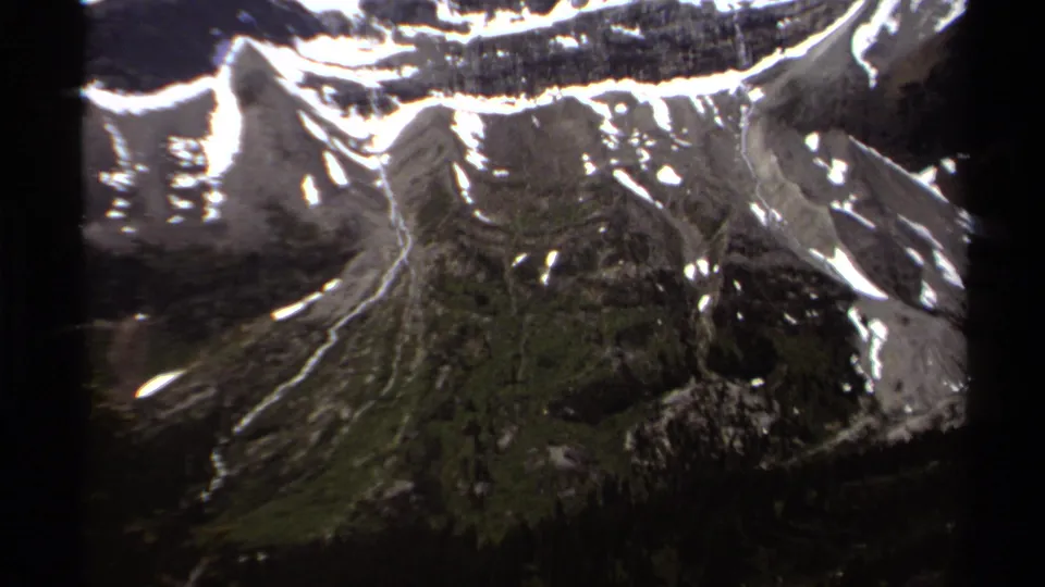 1979 British Columbia frame with steep mountain ridges, snow patches, and dark alpine terrain in soft 8mm color.