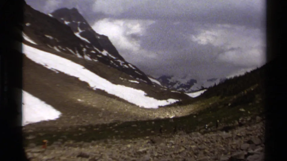 1979 British Columbia mountain-slope view on 8mm film, showing rocky ground, lingering snowfields, and low cloud cover.