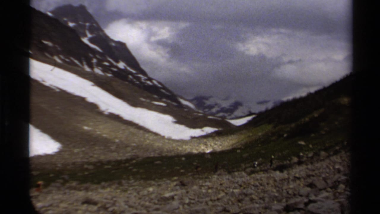 1979 8mm view of a British Columbia mountain valley with lingering snow, rocky terrain and heavy clouds.