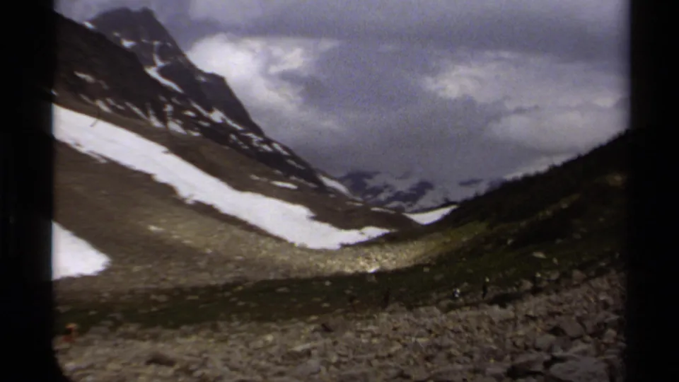 1979 8mm view of a British Columbia mountain valley with lingering snow, rocky terrain and heavy clouds.