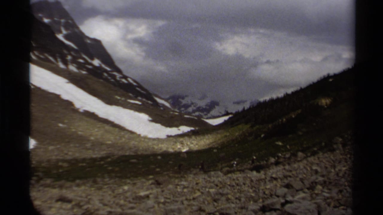 Snow-streaked mountain valley under heavy cloud cover.