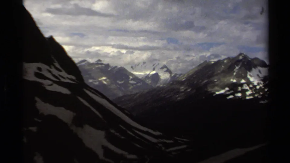 8mm British Columbia mountain panorama with layered ridges, scattered snow and shifting clouds over the peaks.