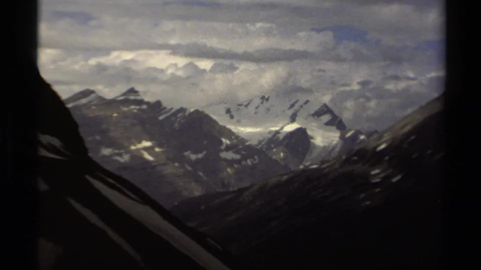 1979 British Columbia 8mm zoom view moving closer to snow-streaked peaks, with bright snowfields and gray clouds filling the background.