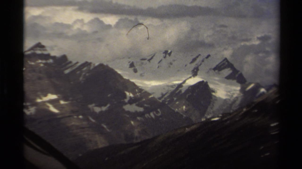 1979 8mm view of snow-covered mountain peaks in British Columbia, seen through dark film-frame borders under a partly cloudy sky.