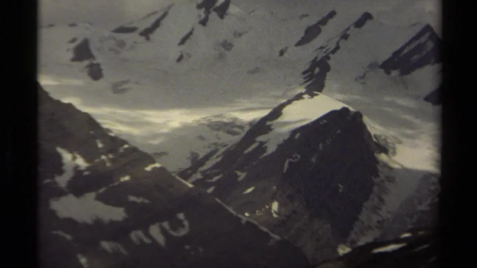 1979 8mm frame of a British Columbia snow-covered alpine slope, with a dark rocky ridge and pale clouded sky.