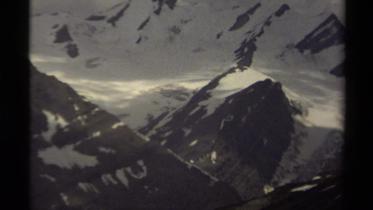 Dark-bordered 8mm frame showing snowy mountain peaks and rocky slopes under cloudy light.