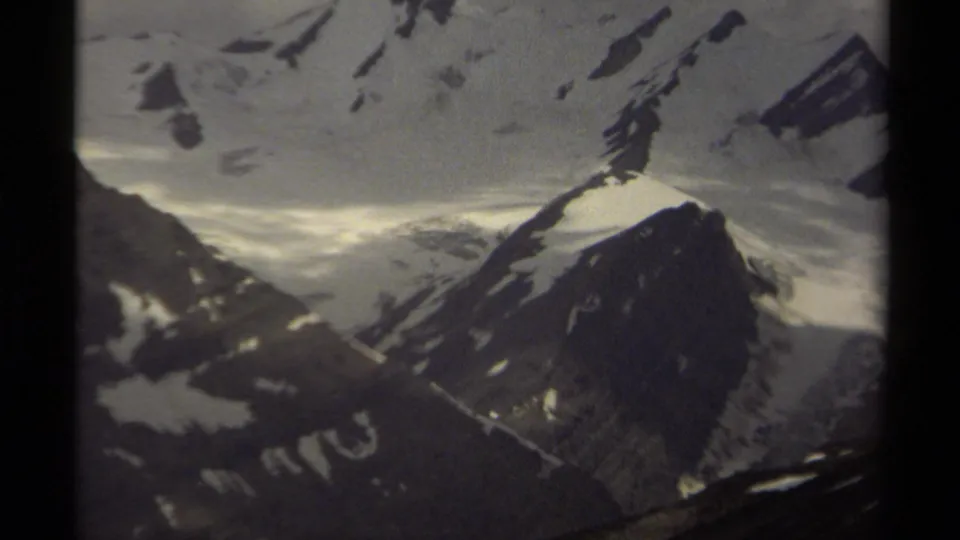 1979 British Columbia 8mm frame with snow-covered mountain ridges, dark rock faces, and muted cloudy sky seen through film borders.