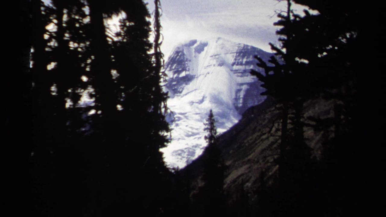 A glacier-covered mountain face appears framed by dark pines in British Columbia home-movie footage from 1979.