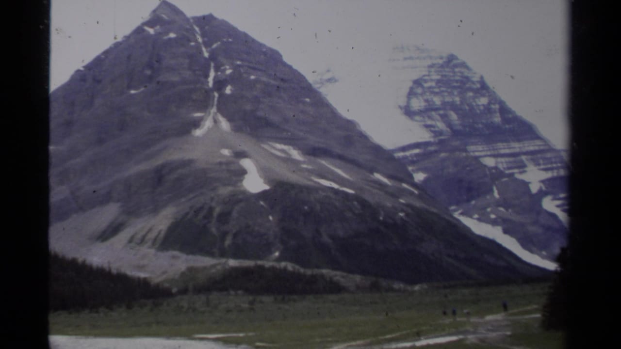 Snow-streaked mountain peaks above a grassy open area.