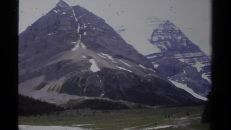 Mountain peaks with snow patches rise above an open meadow in British Columbia 8mm footage.
