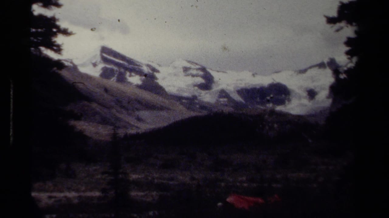 1979 8mm British Columbia mountain view with dark trees, snowy peaks, and a shadowed valley below.