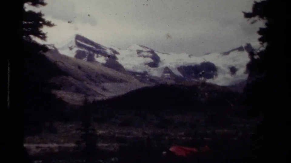 1979 8mm British Columbia mountain view with dark trees, snowy peaks, and a shadowed valley below.