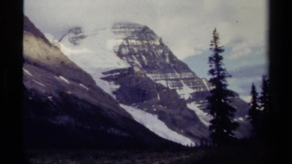 British Columbia 8mm mountain shot showing a steep snow-streaked peak, dark tree silhouettes, and soft faded color.
