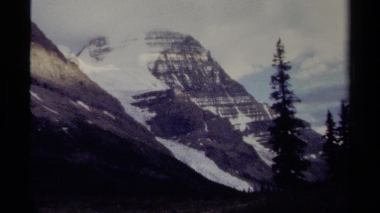 Rocky mountain face with snow patches and evergreen silhouettes in the foreground.