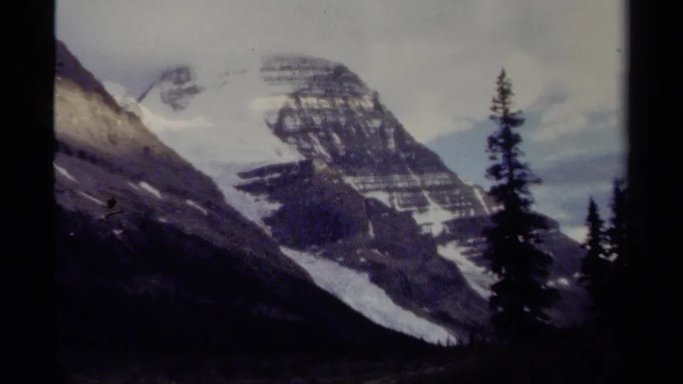 Soft 1979 home-movie frame of a British Columbia mountain slope, snow fields, and dark evergreen trees.
