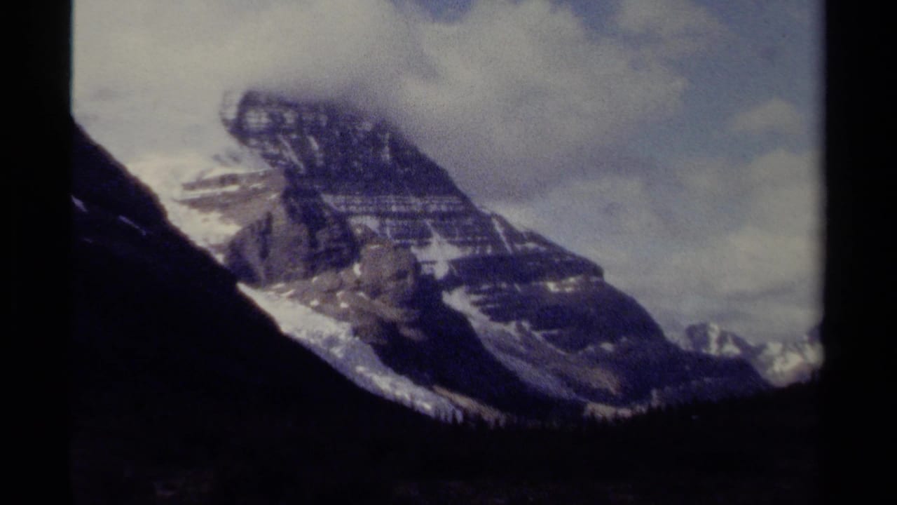 1979 British Columbia 8mm frame showing a rugged snow-capped peak under cloud cover with dark film gate edges.