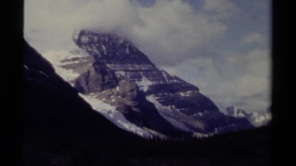 1979 British Columbia 8mm frame showing a rugged snow-capped peak under cloud cover with dark film gate edges.