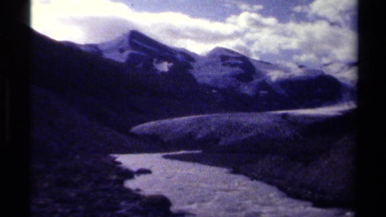 1979 British Columbia 8mm frame showing a glacier or icefield winding below dark alpine slopes and clouded peaks.