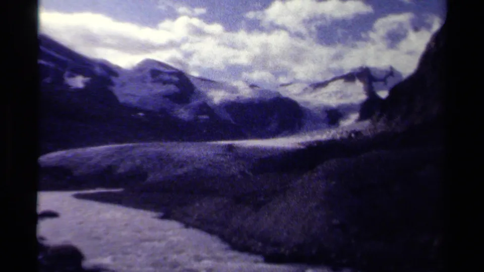 1979 British Columbia 8mm frame showing glacier ice in the foreground with rugged alpine slopes and a clouded mountain backdrop.