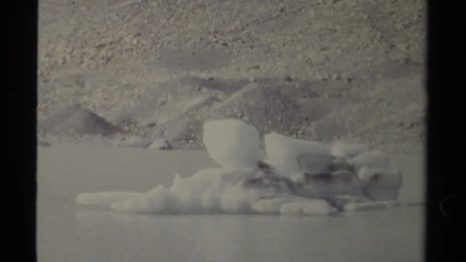 Home-movie view of a pale iceberg or ice fragment on calm water in the British Columbia wilderness.