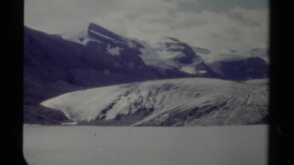 1979 British Columbia landscape frame with snow-covered mountains, a glacier, cloudy sky, and water in the foreground.