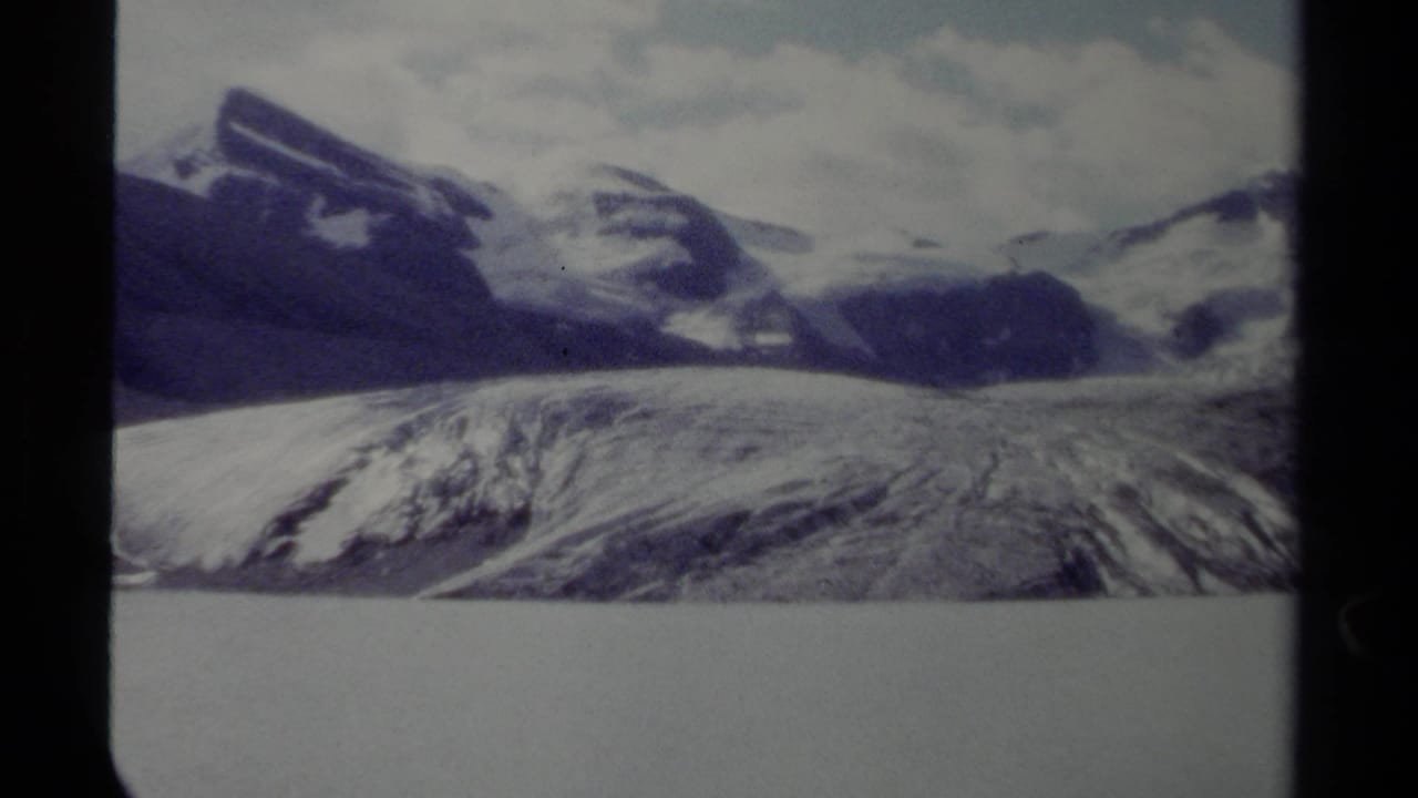 Snowy mountain range and broad glacier seen through dark 8mm film borders.