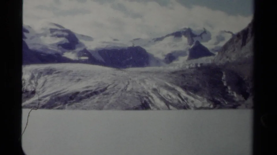 1979 home-movie frame of a glacier and surrounding British Columbia peaks, with a rocky slope entering the view.