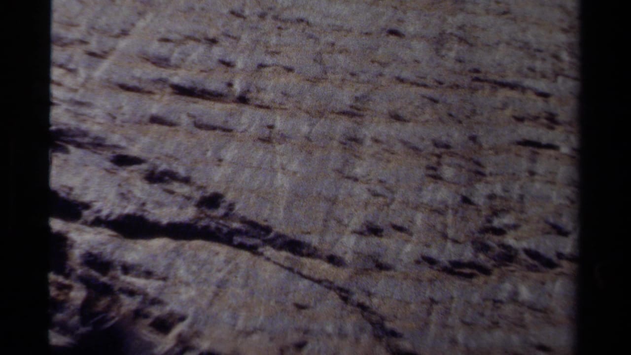 1979 British Columbia 8mm frame showing a close view of a sheer, layered rock wall in daylight.